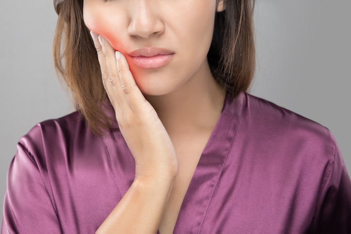 A lady with her hand on the cheek, experiencing toothache or tooth pain.